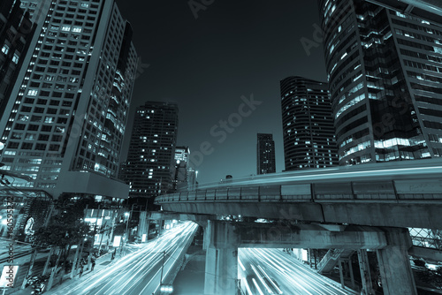 Plakat Fotografia handlowa biurowa powierzchowność. Nocny widok na dole wieżowce ze światłem pośpiechu ruchu, długie exposur w Bangkoku