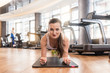 © Kzenon - Front view of a young fit woman smiling while practicing the forearm plank exercise for core strength indoors at the gym