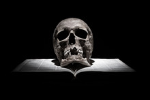 Human Skull On Old Open Book On Black Background Under Beam Of Light