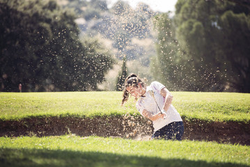 young girl playing golf on a sunny day moving sand in the banker