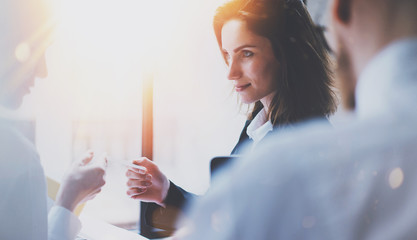 Wall Mural - Group of businessmans on meeting.Business team at working process.Closeup view of young woman giving business card to partner.Blurred background.Horizontal.Flares effect.