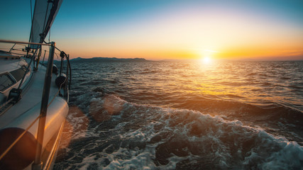 Wall Mural - Slide sailing yacht through the waves of the sea during sunset.