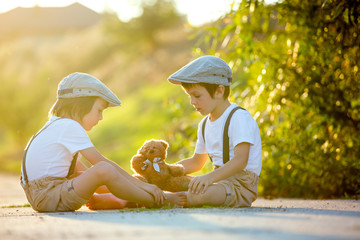 Canvas Print - Sweet children, boy brothers, playing with teddy bear on a small rural path on sunset