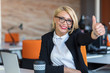 © FS-Stock - Young woman sitting behind desk with thumbs up in an office