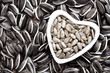 Heart-shaped bowl of dehulled kernels on sunflower seeds background