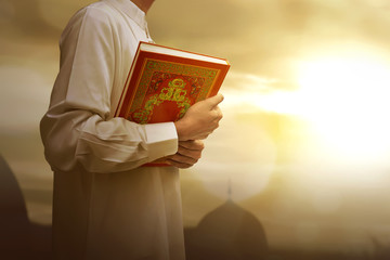 Muslim man in traditional dress holding holy book Koran