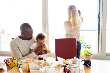 Wall Mural - Young interracial family with little children having breakfast.