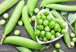 Heart-shaped bowl of fresh harvested green peas on pods background