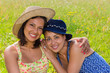 Woman with hat embracing friend in meadow
