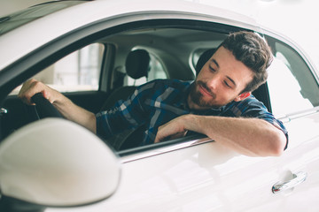 Perfect lines. The young dark-haired bearded man examining car at the dealership and making his choice. Horizontal portrait of a young guy at the car. He is thinking if he should buy it