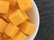 Cubed mild cheddar cheese in a white bowl atop a black slate table top.