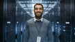 © Gorodenkoff - Portrait of a Curios, Positive and Smiling IT Engineer Standing in the Middle of a Large Data Center Server Room.