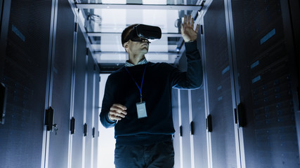 Wall Mural - IT Engineer Wearing Virtual Reality Headset Works with Augmented Reality Software in Data Center. He Wirelessly Interacts with Rack Servers.