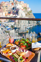 Tasty italian snacks. Fresh bruschettes, cheeses and meat on the board in outdoor cafe with amazing view in Manarola, Italy