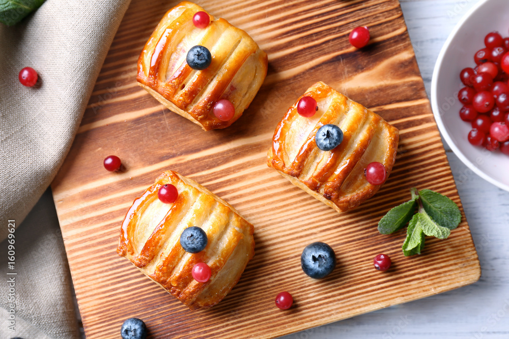 Wooden cutting board with pastries and berries on white table, top view