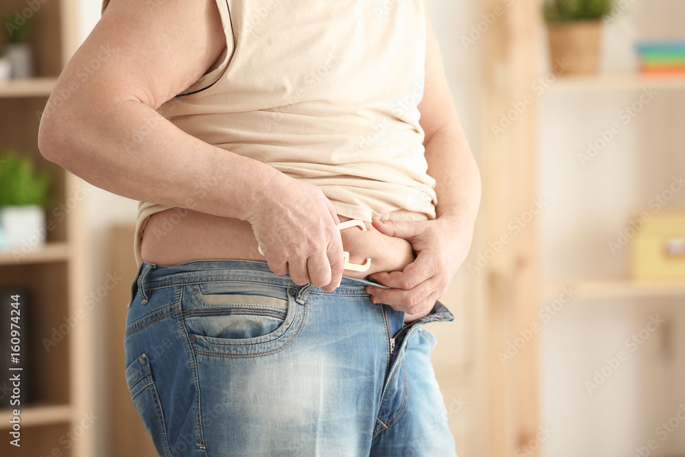 Fat man with measuring caliper at home, closeup. Weight loss concept