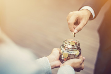 Businessman hand putting money (coin) in the glass jar held by a woman