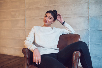Wall Mural - Attractive brunette in a gray sweatshirt sits in a chair.