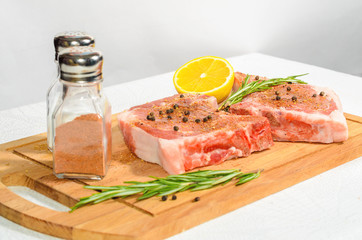 Two appetizing pieces, pork entrecote on a wooden cutting board with salt shaker and pepper and rosemary and lemon