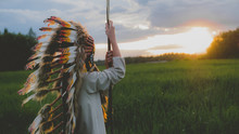 Little Girl Playing Outdoors In The Field, Wearing Indian Headdress, Pretending To Be A Native American. Watching Beautiful Sunset