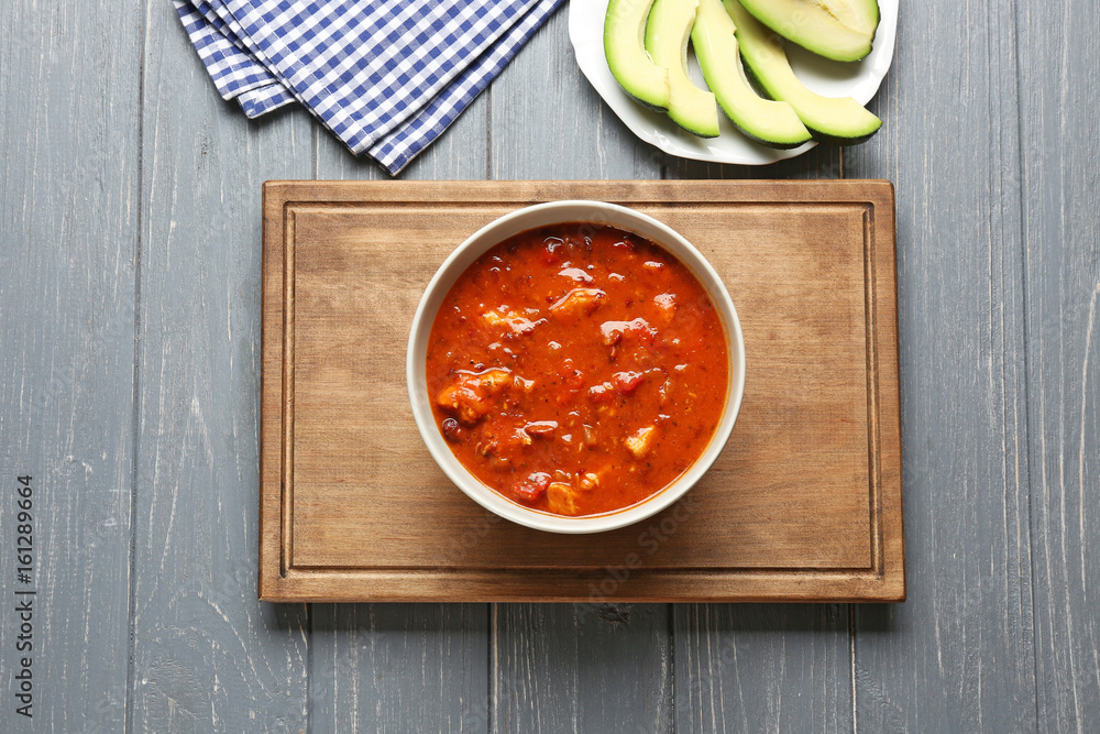 Bowl with delicious chili turkey on wooden board