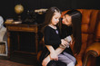 © anna_gorbenko - Mother and daughter hugging and playing together. Pretty little girl on beautiful woman's lap. Girls in black dresses playing in decorated room. Family weekend, beauty day, having fun, love concept.
