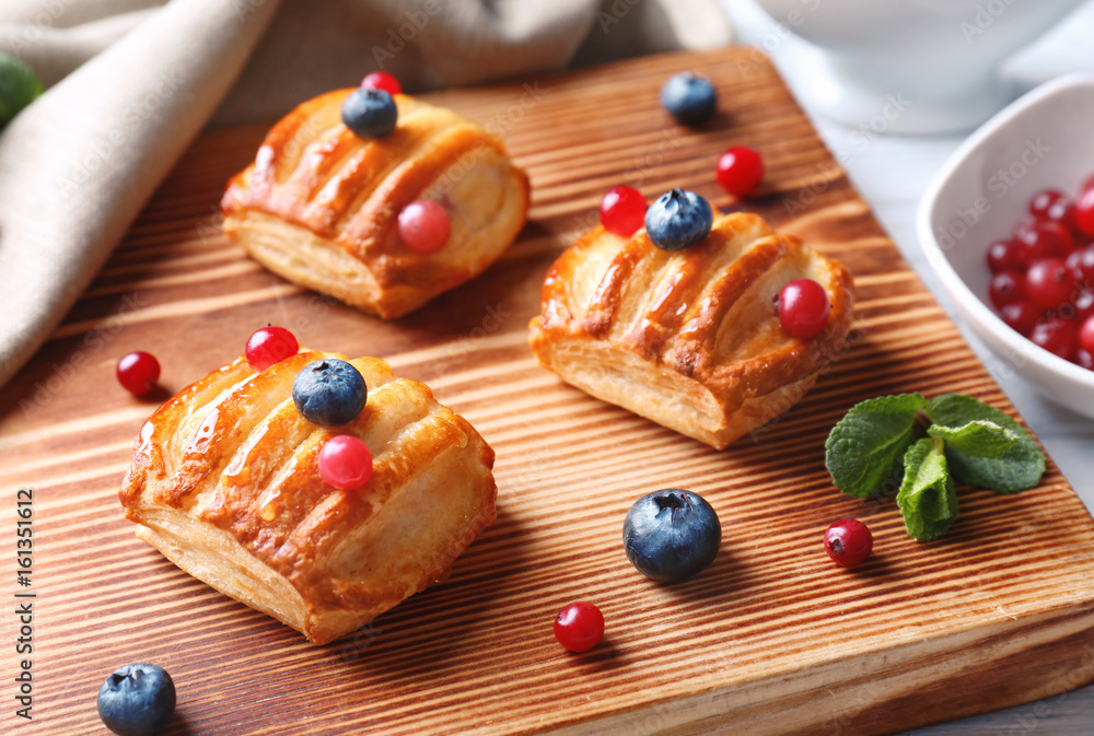Delicious pastries with berries on cutting board, closeup