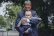 © Westend61 - Portrait of mature businessman holding baby boy outdoors
