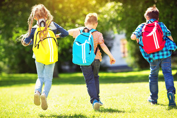 Wall Mural - Children with rucksacks standing in the park near school. Pupils with books and backpacks outdoors