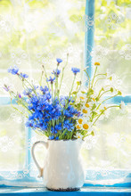 A Bouquet Of Field Flowers Of Cornflowers And Chamomiles In A Pitcher On The Window. Retro, Vintage Style. Home Rural Farming Situation Of The Old Veranda.
