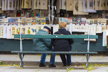 People On A Bench At A Second-hand Book Market On Quay Of River Seine Near Cathedral Notre Dame In Paris