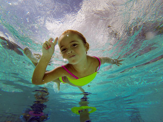 little girl swiming underwater in a pool posing to camera 