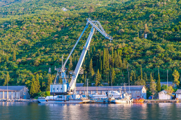 Wall Mural - The old military crane unloads cargo in a small port. Montenegro, Boka-Kotor Bay.