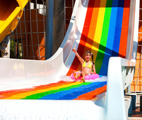 Wall Mural - Swimming pool slides for children on water slide at aquapark . Summer kid holiday outdoor. Happy little girl with super gesture in aqua park slide out on inflatable ring.