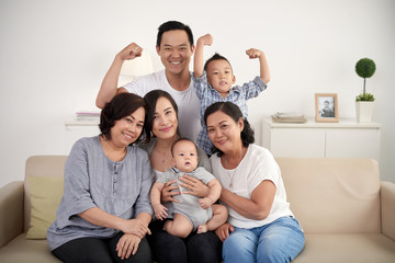 Portrait of big Asian family posing for photo at home: sitting on sofa, looking at camera and smiling happily