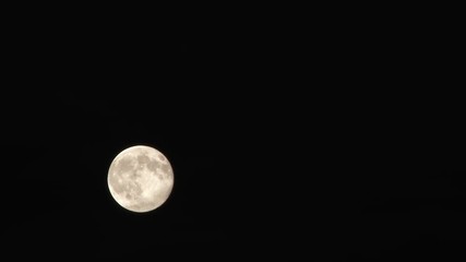 Wall Mural - time lapse of bright full moon passing through night sky then fading to black as clouds fill frame.