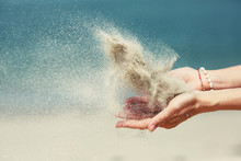 Female Hands Releasing Dropping Sand. Sand Flowing Through The Hands Against Blue Ocean