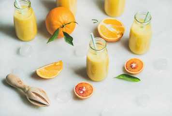 Wall Mural - Healthy yellow smoothie with citrus fruit, ginger, ice in glass bottles over light marble table background, selective focus. Clean eating, vegan, vegetarian, detox, dieting food concept