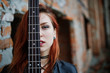 Red haired punk girl wear on black with bass guitar at abadoned place. Portrait of gothic woman musician. Close up face of blackness person with guitar riff.