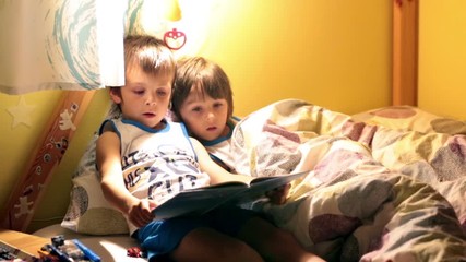 Poster - First grade school boy, reading a book in bed to his younger brother