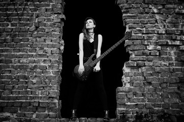 Red haired punk girl wear on black with bass guitar at abadoned place. Portrait of gothic woman musician.