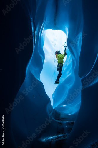Fotografie, Obraz Ice climber viewed through a tunnel in the bottom of a moulin on the Matanuska G