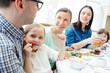 © pressmaster - Cute girl eating fresh strawberry for breakfast with her family near by