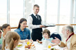© pressmaster - Family of six having meals in restaurant with waiter near by