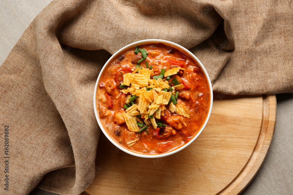Bowl with delicious chili turkey and chips on wooden board