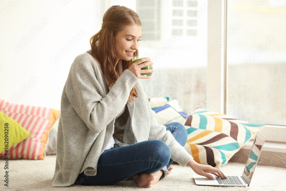Weight loss concept. Beautiful young woman drinking healthy delicious smoothie and using laptop at home