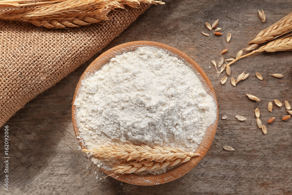 Bowl with flour on wooden table