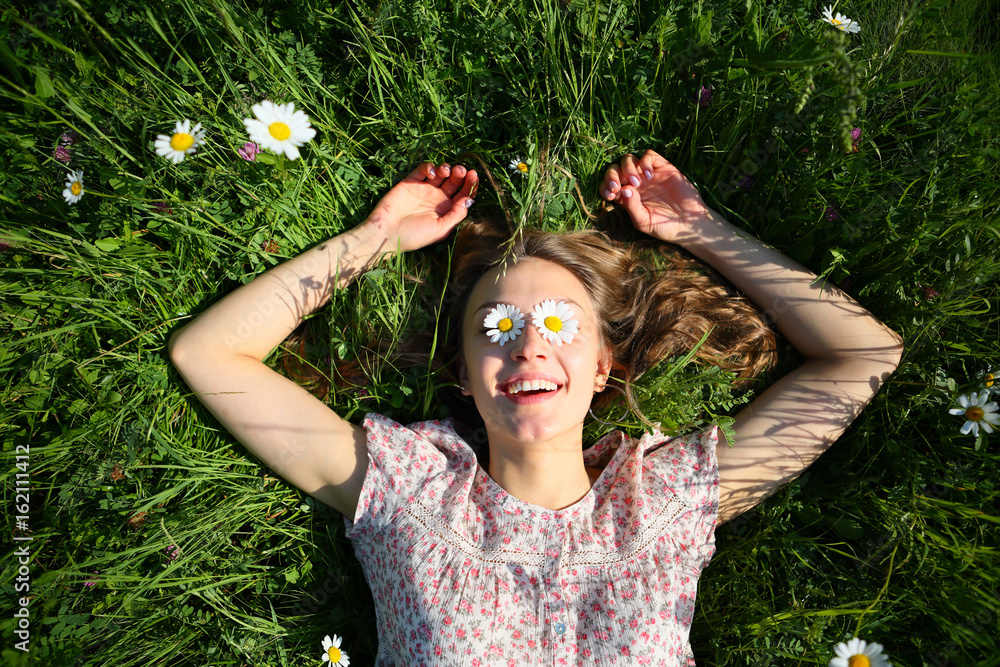 Smiling happy relax young woman lying on fresh green grass in daisies ...