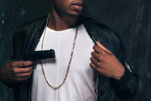 Unrecognizable Black Man Threatens With A Gun Closeup Studio Shoot. Ghetto Gangster With Weapon On Dark Background. Outlaw, Ghetto, Murderer, Robbery Concept