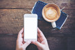 © Farknot Architect - Mockup image of hands holding white mobile phone with blank screen with coffee cups on vintage wooden table in restaurant